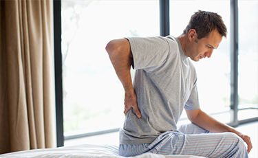 man sitting holding his back as in pain